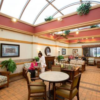 A spacious indoor lobby with seating areas, featuring tables, chairs, and decorative plants.