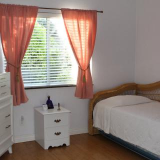 A cozy bedroom with a bed, nightstand, and dresser near a window with pink curtains.