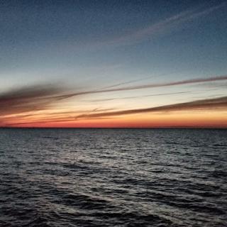 A serene sunset over the calm ocean waters, painting the sky with vibrant hues.