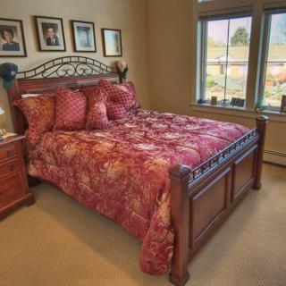 A cozy bedroom featuring a wooden bed with a vibrant patterned comforter, flanked by nightstands and adorned with framed photographs on the wall.