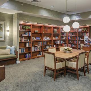 A cozy library setting featuring bookshelves, a reading table with chairs, and ambient lighting.