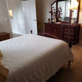 A cozy bedroom with a neatly made bed, a wooden dresser, and warm lighting.