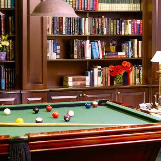 A cozy library room featuring a billiards table and a wall of bookshelves.