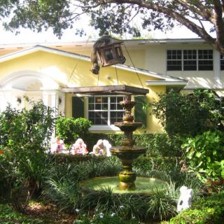 A charming house with a lush garden featuring a fountain and vibrant flowers.