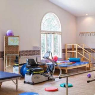 A brightly lit physical therapy room equipped with exercise machines, therapy tables, and various rehabilitation tools.