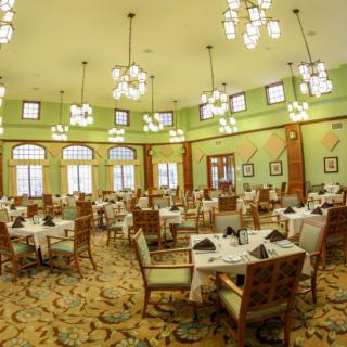 An elegant dining room with neatly arranged tables and chairs, adorned by chandeliers.