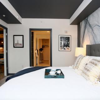 A modern hotel room featuring a neatly made bed, decorative artwork on the walls, and a tray placed on the bed.