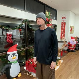 A person standing indoors next to festive Christmas decorations, including a penguin statue.