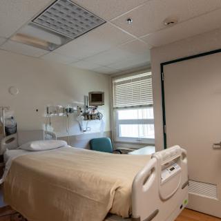 A view of a hospital patient room featuring a bed, medical equipment, and natural light coming through the window.
