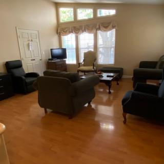 A cozy living room with several chairs, a sofa, and a coffee table arranged around a television. Large windows allow natural light to fill the space.