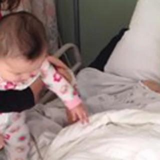 A baby reaching out to a person in a hospital bed.
