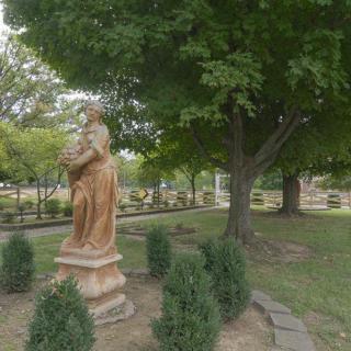 A serene garden area featuring a statue surrounded by lush greenery and trees.