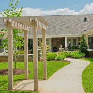 A serene garden pathway leading to a house, featuring a pergola and well-maintained landscaping.
