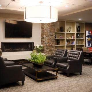 A modern lounge area featuring comfortable leather seating, a large television, and a decorative bookshelf.