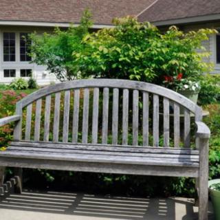 A wooden bench situated in a lush garden with a house in the background.
