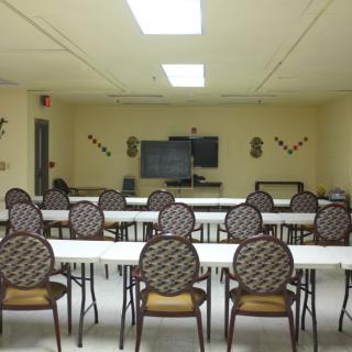 An empty classroom or meeting room with arranged tables and chairs facing a whiteboard.