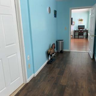 A hallway with blue walls and wood flooring, leading to another room with a desk.