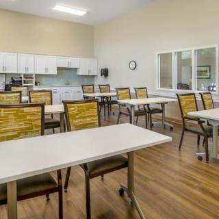 An empty classroom with tables and chairs arranged in rows on a wooden floor.