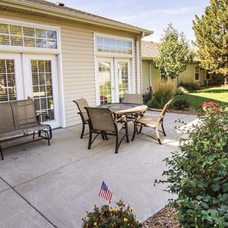 A sunny backyard patio with outdoor furniture and a small American flag in the garden.