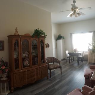 A cozy living and dining area featuring a china cabinet, chairs, and a ceiling fan with ample natural light.