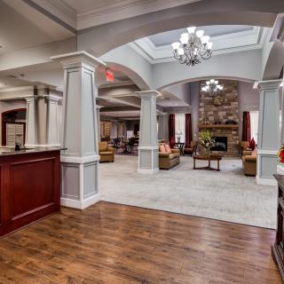 A spacious and elegantly designed hotel lobby featuring a reception desk, seating area, chandelier, and fireplace.