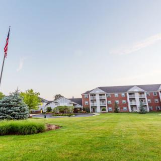 A scenic view of an apartment complex with a spacious lawn and a flagpole under a clear sky.