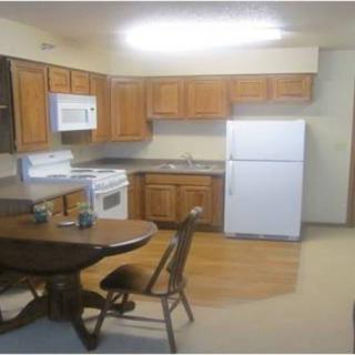 A cozy kitchen and dining area with wooden cabinets, a white refrigerator, stove, microwave, and a small dining table with chairs.