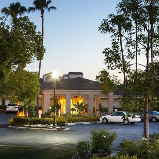 A hotel entrance surrounded by trees and a parking lot in the evening.