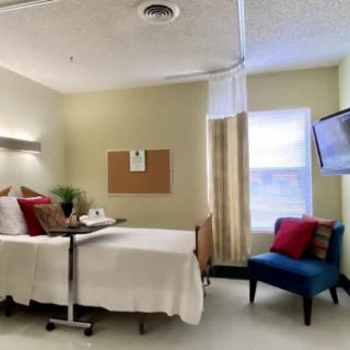 A modern hospital room with a bed, chair, and wall-mounted television.