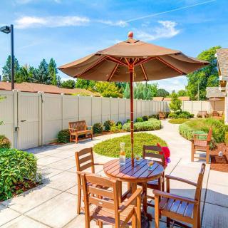 A well-maintained patio area with wooden furniture and a large umbrella, surrounded by a landscaped garden.