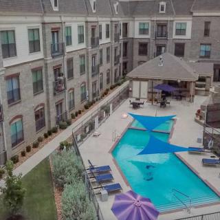 A modern apartment complex features a central swimming pool surrounded by outdoor seating and shaded areas.