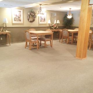 An indoor dining area with tables and chairs, featuring carpeted flooring and subtle wall decorations.
