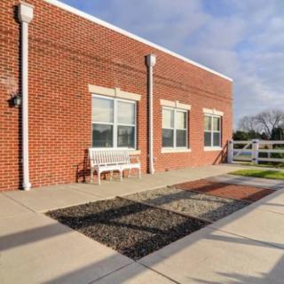 A brick building with large windows, a white bench, and a fenced area under a blue sky.