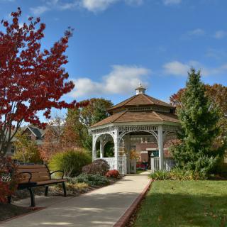 A scenic park setting with a gazebo, surrounded by autumn foliage and a clear blue sky.