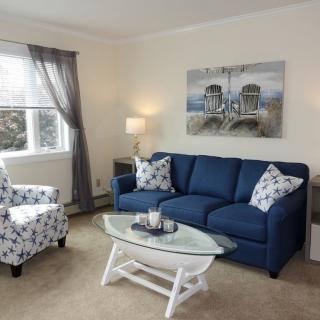 A cozy living room featuring a blue sofa, patterned armchair, and a glass-top coffee table.