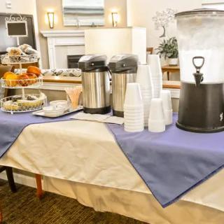 A refreshment table set up with coffee, water, snacks, and disposable cups.