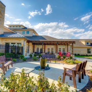A sunny day view of a landscaped outdoor patio area with seating and a building in the background.