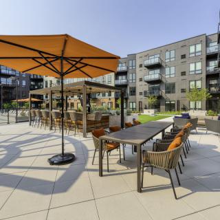 An outdoor patio with tables and chairs under large umbrellas, set within an apartment complex.