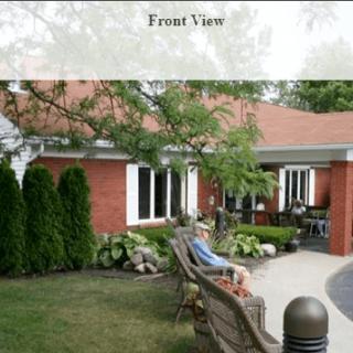 A front view of a red brick house with a garden and bench.