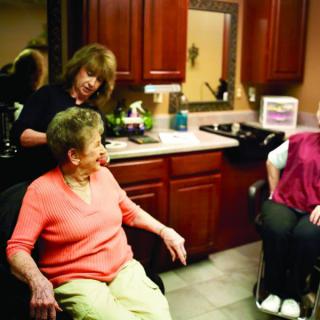 Two elderly women having a conversation in a hair salon as a hairdresser attends to one of them.