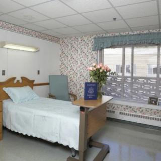 A clean and well-lit hospital room with a bed, table, and flowers by the window.