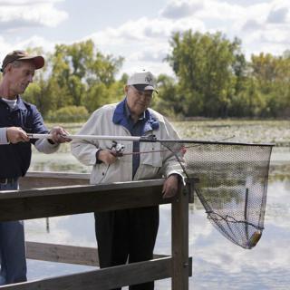 Two people fishing from a pier by a lake.