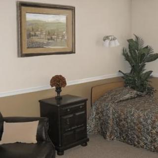 A cozy bedroom with a bed, nightstand, and armchair, featuring wall art and decorative plants.
