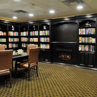 A cozy library room featuring bookshelves, a table with chairs, and a fireplace.