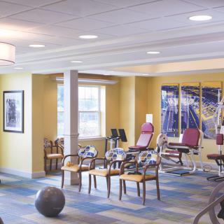 A well-lit exercise room with fitness equipment and chairs.