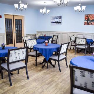 A cozy dining room with tables and chairs, adorned with blue tablecloths and elegant chandeliers.