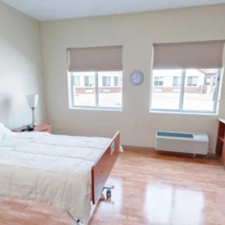 A clean and minimalist hospital room with a single bed and large windows allowing daylight to fill the space.