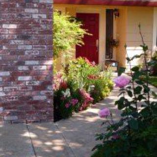 A charming garden pathway leads to a red door, surrounded by blooming flowers and greenery.