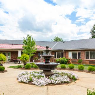 A serene courtyard featuring a central fountain surrounded by lush greenery and colorful flowers.