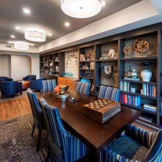 A modern library with a dining table and bookshelves, featuring comfortable seating and decorative items.